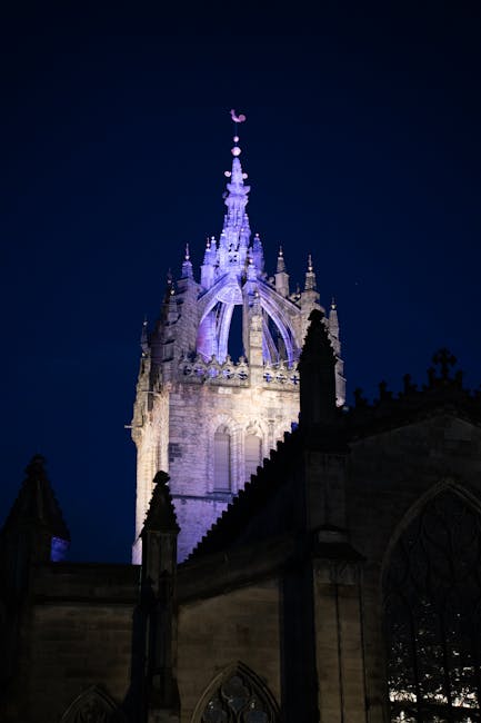 A street scene near St Giles Circus showing several multi-storey buildings with a variety of architectural styles, including brick and ornate facades, some with bay windows and decorative elements. In the foreground, a light blue van belonging to Man with Van St Giles is parked on the street, positioned near loading bays used for home relocation and furniture transport services. The van is adjacent to the pavement, beside a row of bike racks, with some movement of boxed and wrapped furniture visible, suggesting ongoing packing and loading for a house removal. There are a few pedestrians and street signage present, with cloudy daylight illuminating the scene, reflecting typical urban loading and loading area conditions as part of a professional moving process involved in house removals and relocation services.